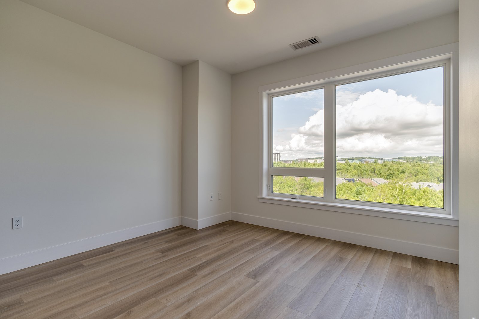 Bedroom with a wide window overlooking the treeline and rooftops